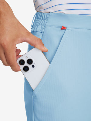 Hand placing an iPhone into pocket of lightweight flat front casual trousers in light blue.