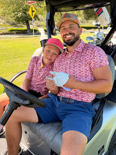 A father and son wearing PINK DONUT Performance Jersey Print Polos are sitting in a golf cart