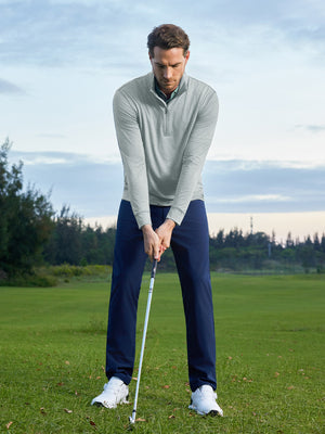 Model on grass under blue sky, leaning on golf club, wearing quarter zip melange pullover in lunar rock melange.
