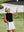 Model holding golf club on outdoor course wearing black women's moisture-wicking mock neck sleeveless golf tops